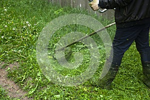 Mows the grass with a hand-held lawn mower. The gardener is cutting the lawn