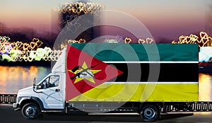 Mozambique flag on the side of a white van against the backdrop of a blurred city and river. Logistics concept