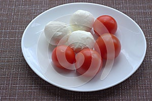 Mozzarella balls lie with small tomatoes on a white plate. Good choices for dieters