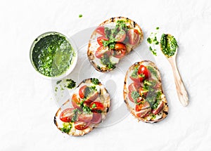 Mozzarella cheese, cherry tomatoes and arugula pesto bruschetta on light background, top view. Arugula pesto and sandwiches - tast