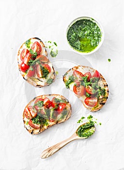 Mozzarella cheese, cherry tomatoes and arugula pesto bruschetta on light background, top view. Arugula pesto and sandwiches - tast