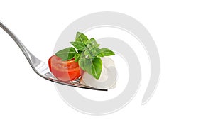 Mozzarella on a fork close up. Mozzarella cheese with tomato and green basil leaf isolated on a white background. Copy space