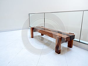 mpty brown long thick wooden bench seat on a white wall near the glass partition decoration inside the modern building.