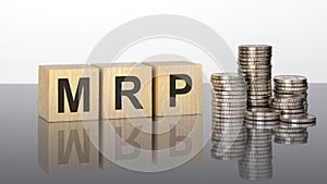 MRP - text on wooden cubes on a cold grey light background with stacks coins