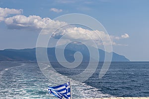 Mt Athos - National flag of Greece waving in the wind. Scenic view from tourist boat on Mount Athos, Chalkidiki, Greece