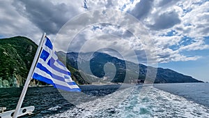Mt Athos - National flag of Greece waving in the wind. Scenic view from tourist boat on Mount Athos, Chalkidiki, Greece