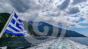 Mt Athos - National flag of Greece waving in the wind. Scenic view from tourist boat on Mount Athos, Chalkidiki, Greece