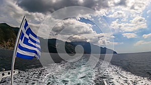 Mt Athos - National flag of Greece waving in the wind. Scenic view from tourist boat on Mount Athos, Chalkidiki, Greece