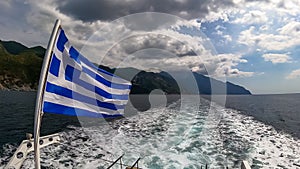 Mt Athos - National flag of Greece waving in the wind. Scenic view from tourist boat on Mount Athos, Chalkidiki, Greece