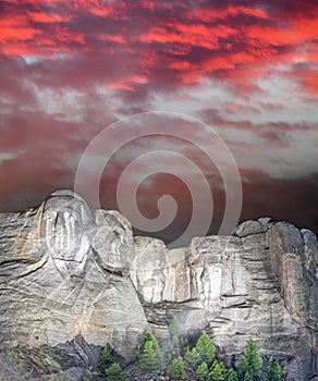 Mt. Rushmore national memorial park in South Dakota at night, presidents faces illuminated against sunset sky