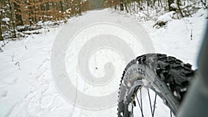 MTB cycling within dark winter day on the snowy road in forest. Slippery snowy surface and lots of icy places.