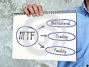 MTF Multilateral Trading Facility on Concept photo. Young Man Holding a notepad
