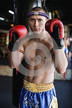 Muay thai fighter standing with hands on red gloves at gym
