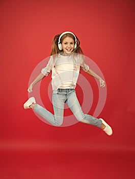 So much fun. Girl listening music modern gadget. Kid happy with wireless headset dancing jumping. Stereo headphones. Kid