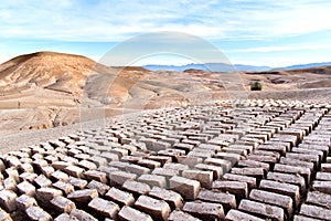 Mud bricks drying in the Moroccan desert with sand dunes and the foothills of the Atlas Mountains in the background