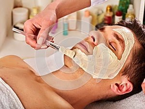 Mud facial healing mask of man in spa salon.