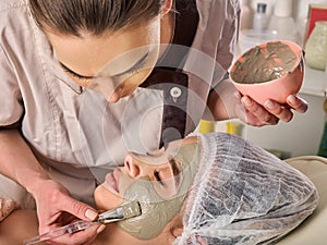 Mud facial mask of woman in spa salon. Face massage.