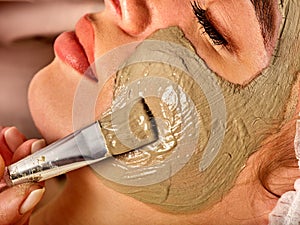 Mud facial mask of woman in spa salon. Massage with clay full face.