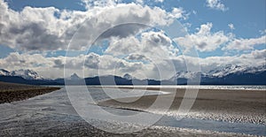 Mud flat tidal outflow at low tide under cumulus clouds on Homer Spit in Homer Alaska USA