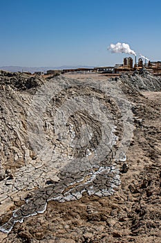 Mud flow from geothermal volcano pots at Salton Sea with energy generating plant in the background