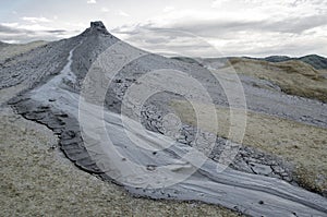 Mud volcano eruption in arid land with grey clouds in background