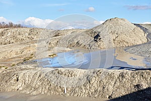 A mud volcano and a stream of grey clay from an eruption and gas escape. Cracked soil surface. Texture of a mudflow