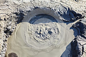 A mud volcano and a stream of grey clay from an eruption and gas escape. Cracked soil surface. Texture of a mudflow