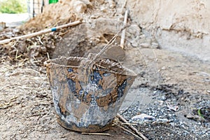 A muddy bucket being used to apply mud plaster to a traditional stone house