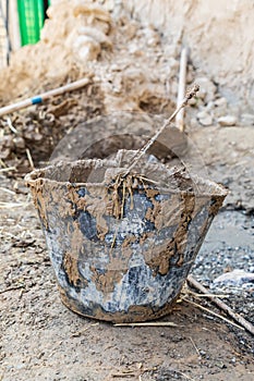A muddy bucket being used to apply mud plaster to a traditional stone house