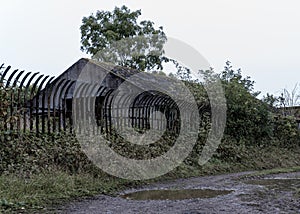 A muddy footpath next to abandoned buildings. Protected by a high metal fence. Saxons Lode Oil Storage Facility, Worcestershire,