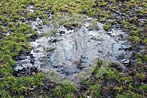 A muddy puddle of water on a grass football pitch