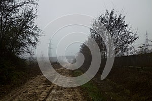 Muddy road next to a railroad track on a foggy day in the italian countryside