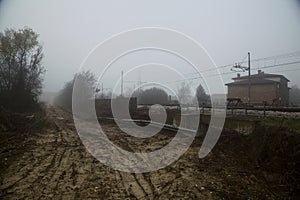 Muddy road next to a railroad track on a foggy day in the italian countryside