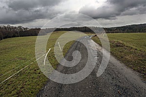 Muddy road between pastures under storm clouds