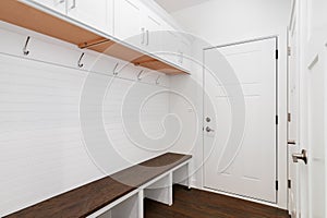 A mudroom with a bench, white cabinets, and coat hooks.