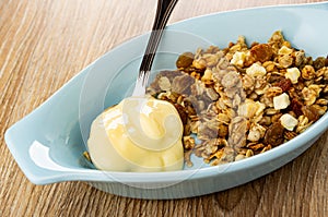 Muesli with apple and raisin, spoon with yogurt in plate on table