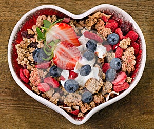 Muesli with berries and yogurt in heart shaped bowl.