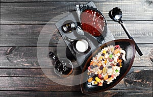 Muesli bowl with yogurt, granola, sliced banana, cashew, almonds, cranberries, nuts, dried fruits mix on dark wooden table