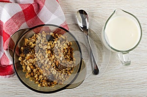 Muesli in brown bowl, napkin, spoon, pitcher with yogurt. Top view