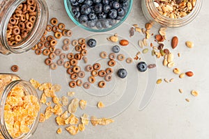 Muesli and cereals are scattered with jars with berries of cherries, blueberries and sweet cookies on a light background,