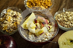 Muesli with dried fruit, milk and sliced red apple on wooden table