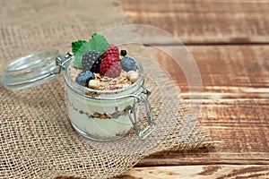 Muesli granola with yogurt and fresh raspberries, blueberries and blackberries, nuts in a glass jar on a wooden background.