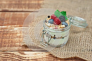 Muesli granola with yogurt and fresh raspberries, blueberries and blackberries, nuts in a glass jar on a wooden background.