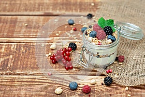 Muesli granola with yogurt and fresh red currant berries raspberries blueberries and blackberries, nuts in a glass jar on a wooden