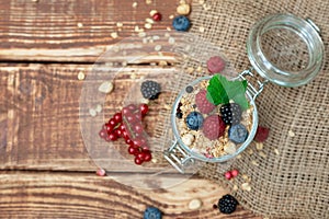 Muesli granola with yogurt and fresh red currant berries raspberries blueberries and blackberries, nuts in a glass jar on a wooden