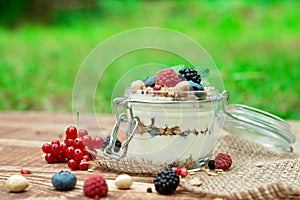 Muesli granola with yogurt and fresh red currant berries raspberries blueberries and blackberries, nuts in a glass jar on a wooden