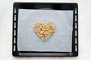Muesli heart on parchment paper on baking sheet and marble kitchen table, above. Made homemade granola, healthy breakfast