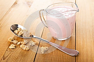 Muesli in spoon, pitcher with yogurt, scattered granola on wooden table