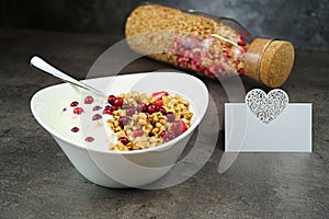 Muesli with srawberry and cranberry with yogurt in white bowl on grey background. Name card with heart.