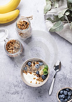 Muesli with vegetarian yogurt, banana and blueberries in a bowl on a gray texture background. Healthy and dietary homemade granola
